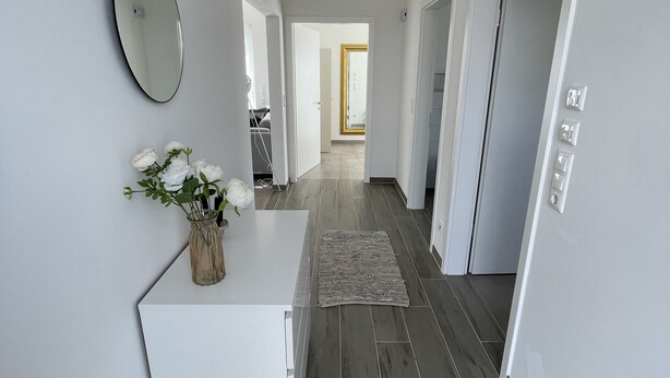 En moderne gang med et hvidt receptionistskrivebord, et spejl og en vase med blomster.