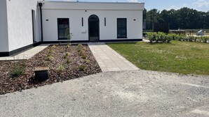 En moderne bygning med en hvid facade, en hovedindgang med en bue og et lille område med græs og buske.