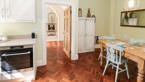 Een keuken met houten vloer, witte kasten, een eettafel met stoelen en een hanglamp.