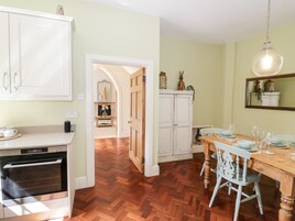 A kitchen with wooden flooring, white cabinets, a dining table set with chairs, and a hanging light fixture.