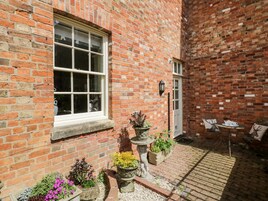 A brick building with a large window and a door, surrounded by potted plants and outdoor furniture.