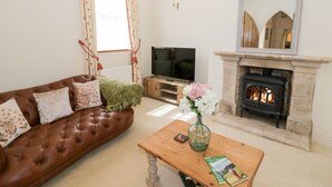 Een woonkamer met een bruine leren bank, een houten salontafel met een bloevas, een televisie en een stenen open haard.