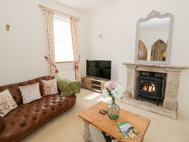 A living room with a brown leather sofa, a wooden coffee table with a vase of flowers, a television, and a stone fireplace.