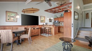A spacious living area with a dining table, chairs, a kitchen, and a staircase. - Aloha Condos, Keauhou Resort, Condo 108, Ocean View, AC (Kailua Kona)
