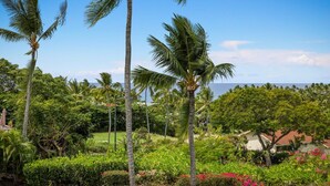 A tropical garden with palm trees and lush greenery, a clear blue sky, and a view of the ocean. - Aloha Condos, Keauhou Resort, Condo 108, Ocean View, AC (Kailua Kona)