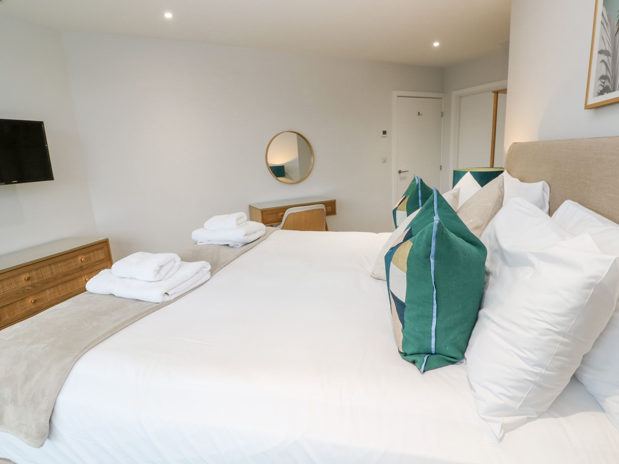 Un lit bien fait, avec du linge de lit blanc, un plaid beige et des coussins verts.