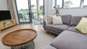 Una sala de estar moderna con un sofá gris, una mesa de centro de madera y un televisor sobre un mueble de madera.