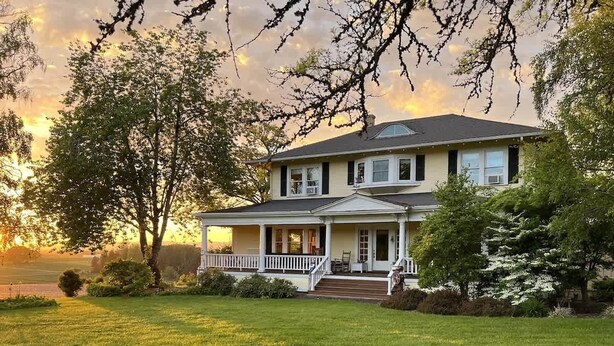 A two-story house with a front porch, surrounded by trees and a grassy lawn. - Barn Owl Hill - Historic Farmhouse Vineyard Views (Rickreall)
