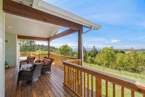 Un terrazzo in legno con mobili da esterno, una ringhiera e vista su un paesaggio boschivo.