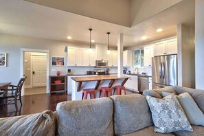 A modern kitchen with white cabinets, a central island with stools, stainless steel appliances, and pendant lighting.