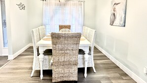 A dining area with a white table and wicker chairs, a light fixture above, and a painting on the wall. - "Bayou Breeze" Private Pool (Heated) Gorgeous Home! Bikes, Game room (Navarre)