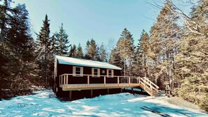 A cabin with a wooden deck and a staircase leading to a covered area.