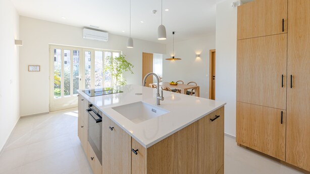 A modern kitchen with a central island, wooden cabinets, and pendant lighting. - The Olive Poolhouse (Split)