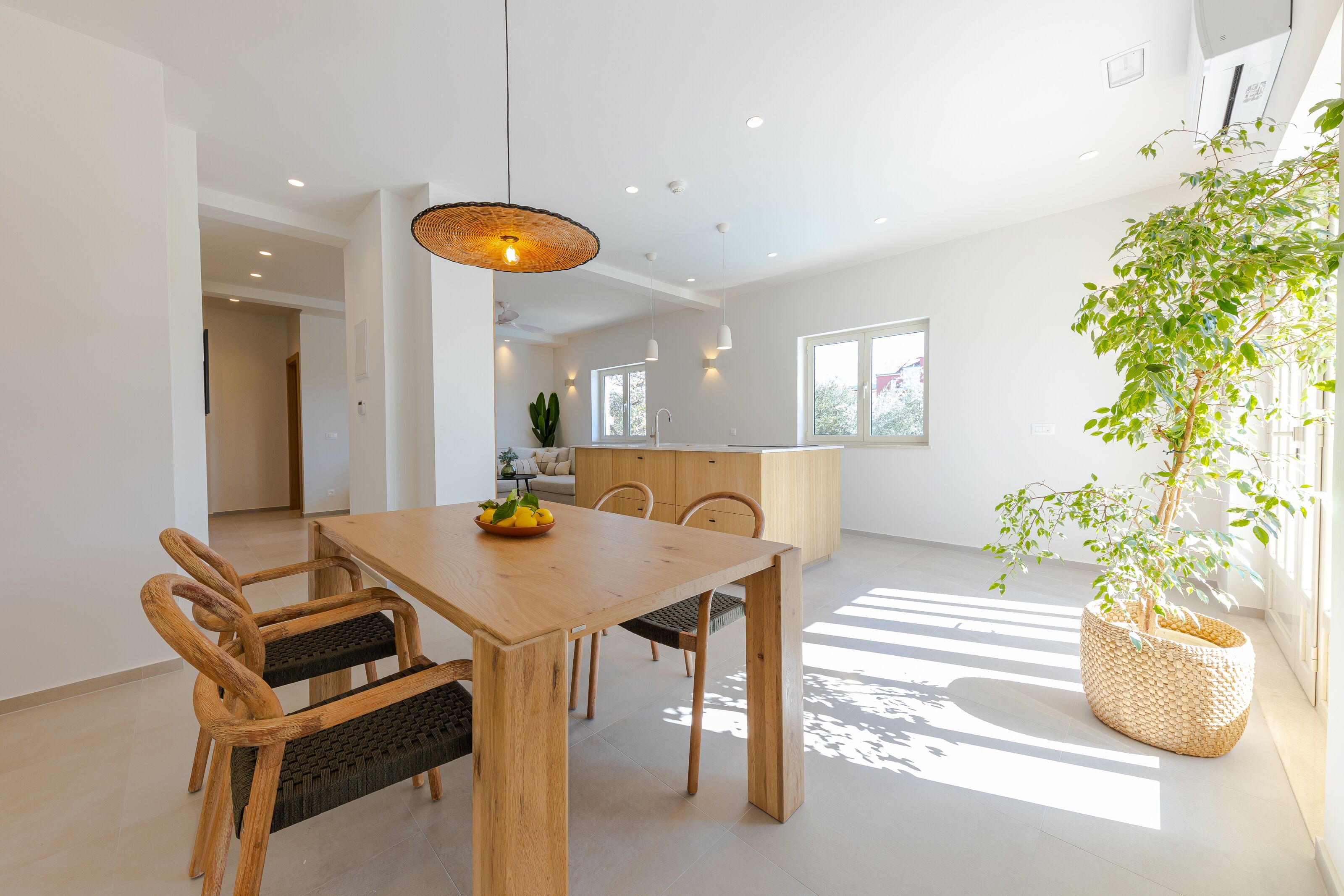 A modern dining area with a wooden table and chairs, a hanging light fixture, and a potted plant.