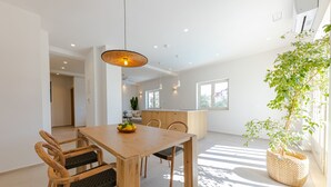 A modern dining area with a wooden table and chairs, a hanging light fixture, and a potted plant. - The Olive Poolhouse (Split)