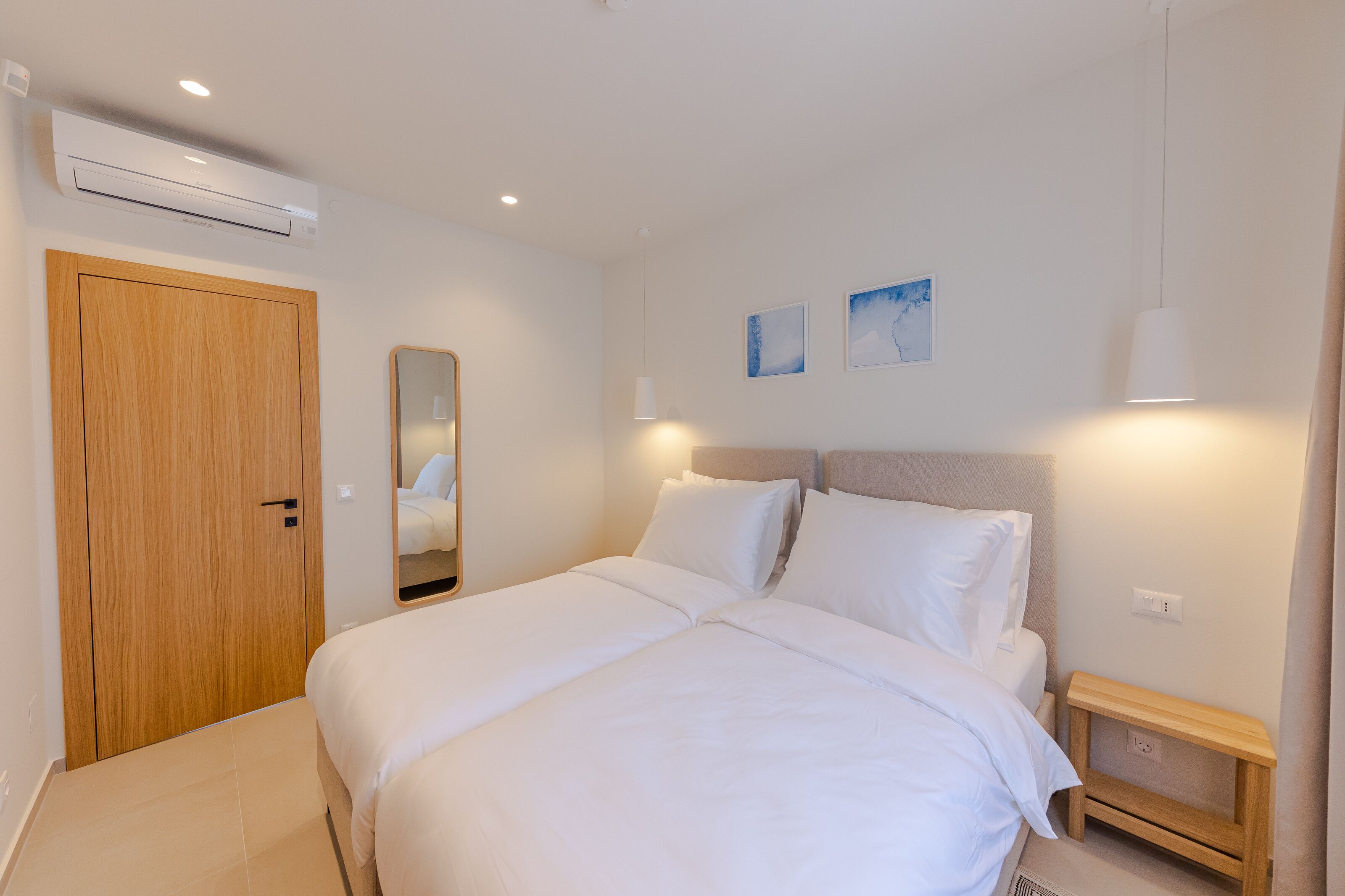 Un dormitorio con una cama doble, un armario de madera, una mesita de noche y un aire acondicionado de pared.