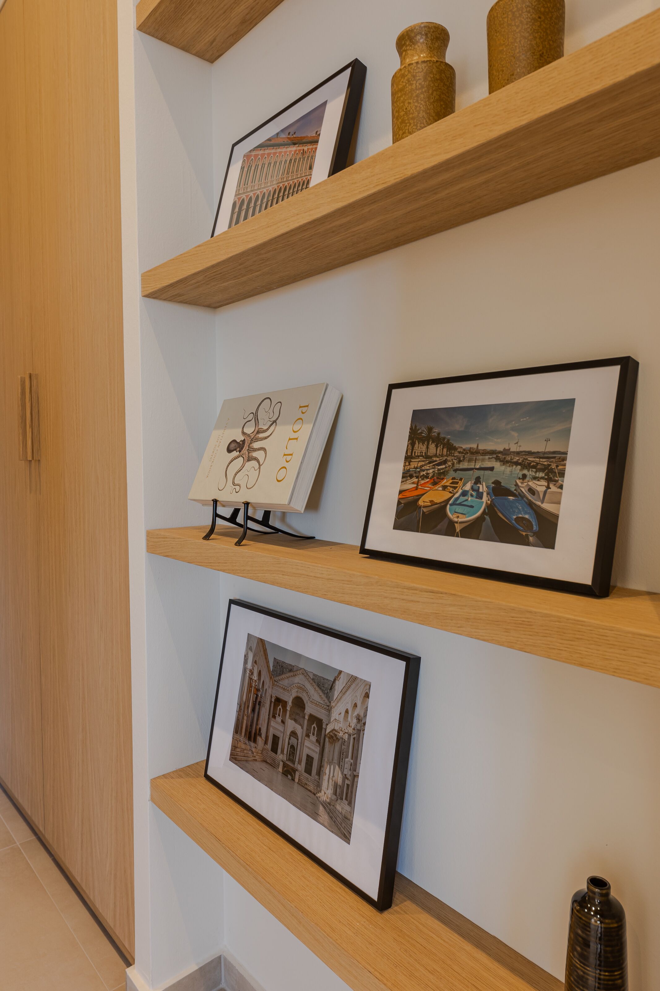 Un mur orné de trois étagères en bois où sont exposés des œuvres d’art encadrées et des objets décoratifs.