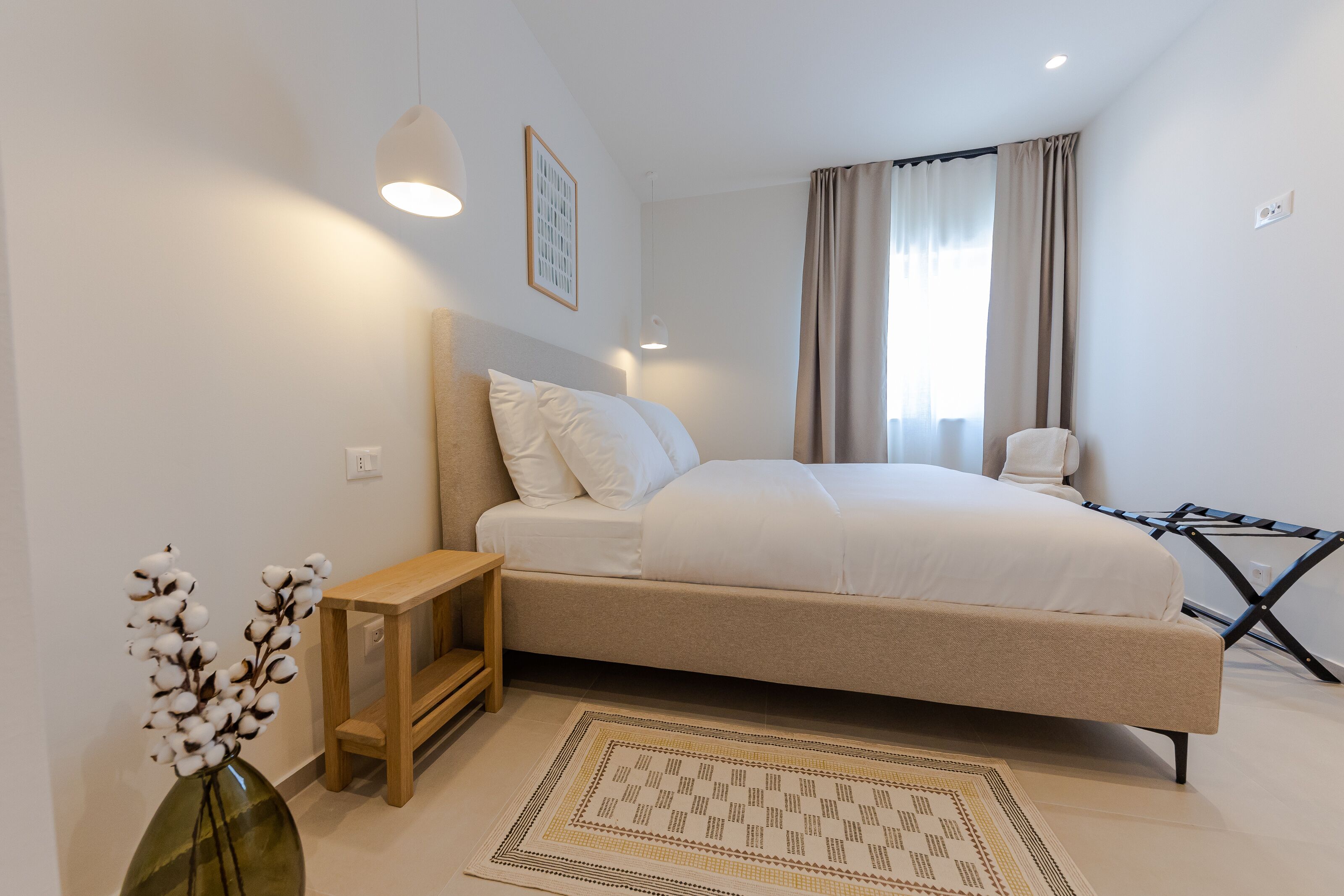 A bedroom with a bed, bedside table, lamp, and a vase with flowers.