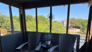 A covered outdoor seating area with two Adirondack chairs, a small table, and a potted plant. - Beachside home in the heart of Duck, NC and walkable to the ocean! (Kitty Hawk)