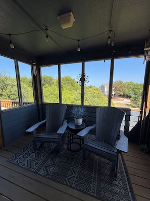 A covered outdoor seating area with two Adirondack chairs, a small table, and a potted plant. - Beachside home in the heart of Duck, NC and walkable to the ocean! (Kitty Hawk)