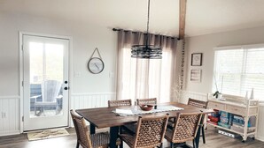 Un coin repas avec une table en bois et des chaises en osier, un luminaire suspendu et une fenêtre avec des rideaux.