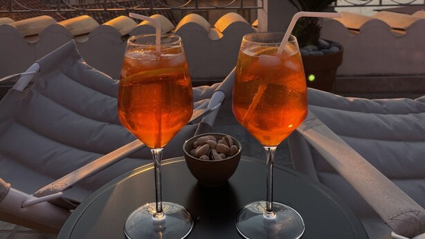 Two drinks on a table with a sunset view through a metal fence.