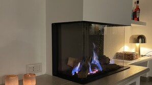 A modern fireplace with a glass enclosure, a stone bench, and a small shelf with candles.