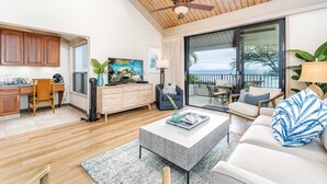 A spacious living room with a large window, a ceiling fan, and a view of the outdoors. - Breathtaking Ocean Views Kahana Village 40 2BR/2BA Condo Pool, Beach Access (lahaina)