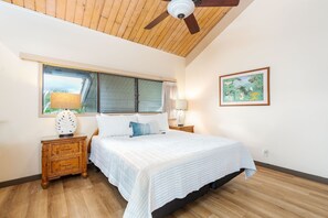 A bedroom with a large bed, wooden nightstands, a ceiling fan, a window with blinds, and a framed picture on the wall.