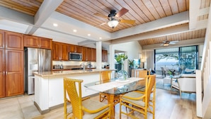 A modern kitchen with wooden cabinets, stainless steel appliances, and a glass dining table with wicker chairs. - Breathtaking Ocean Views Kahana Village 40 2BR/2BA Condo Pool, Beach Access (lahaina)