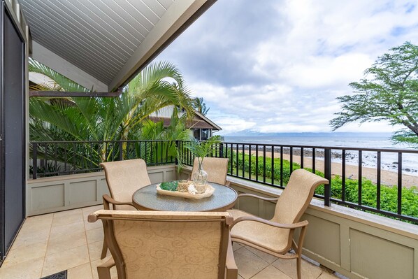 A balcony with a table and chairs, overlooking a beach and ocean.