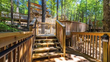 A wooden staircase leading to a wooden deck surrounded by trees.