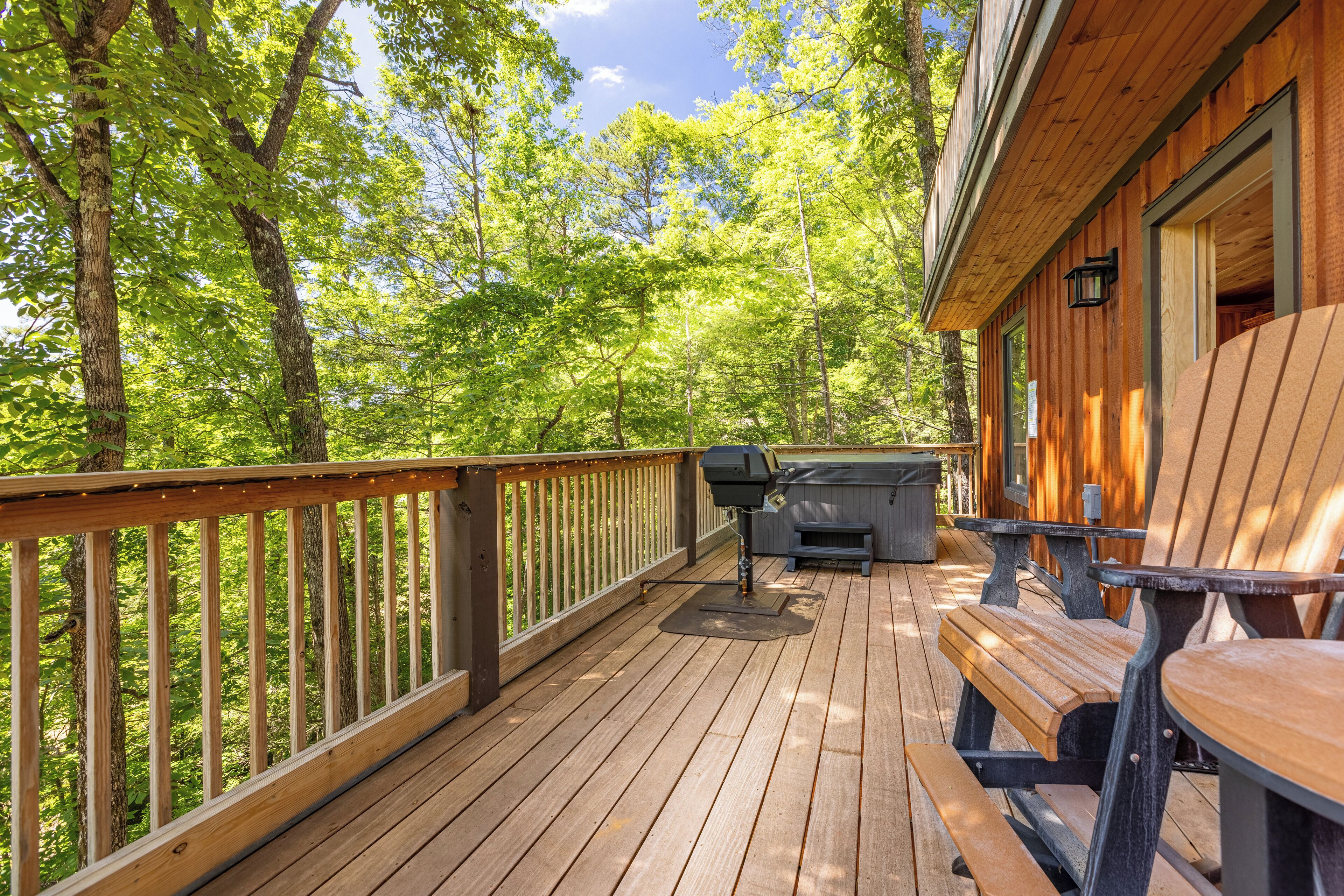 A wooden deck with a grill and seating area, surrounded by trees.