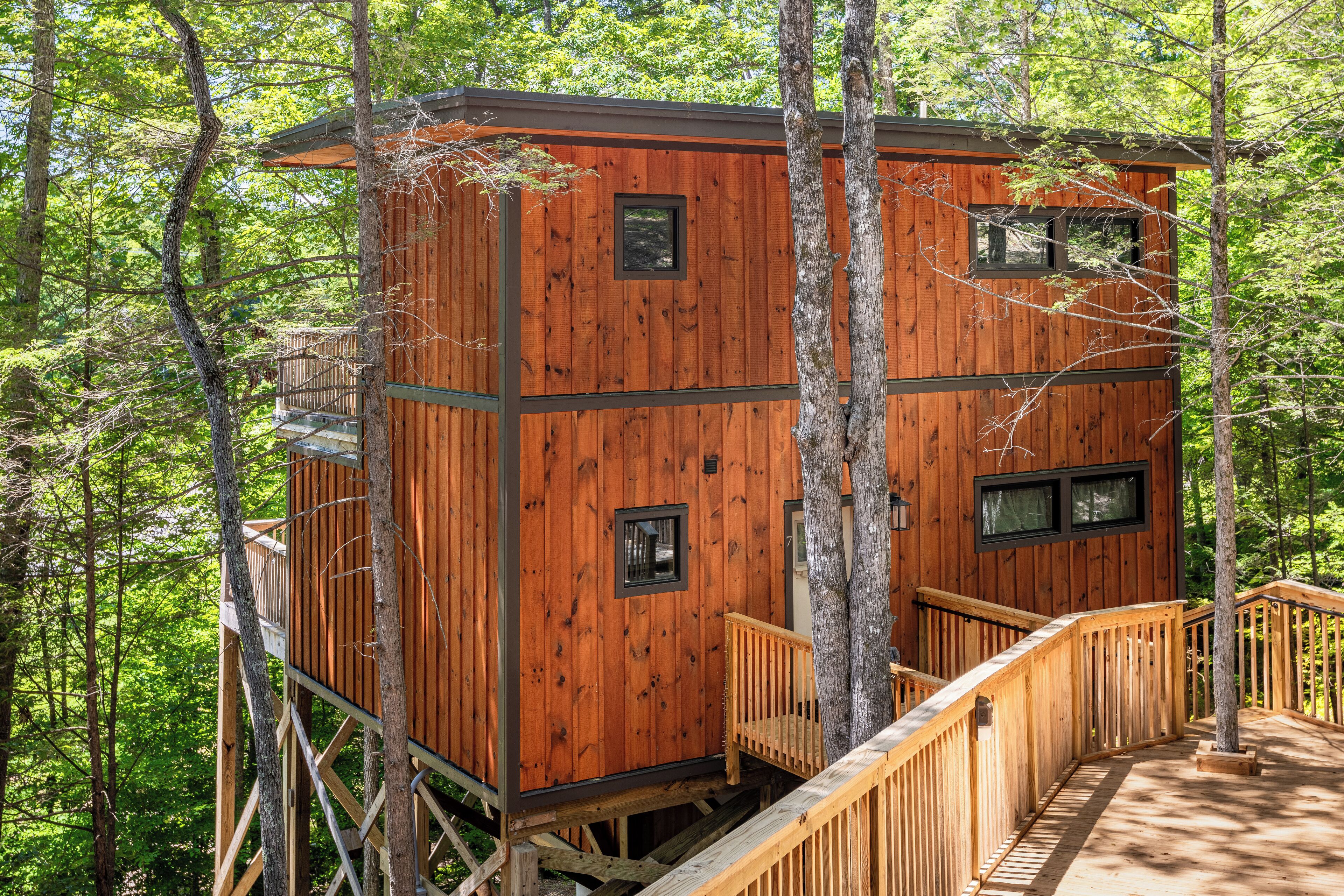 A wooden cabin with a deck and multiple windows, surrounded by trees.