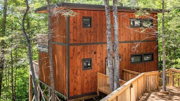 A wooden cabin with a deck and multiple windows, surrounded by trees.