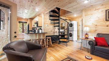 A cozy cabin interior with a spiral staircase, wooden floors, a sofa, and a dining area.