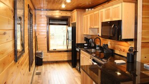 Une cuisine rustique, située dans une cabane en bois, équipée d’un réfrigérateur, d’un four à micro-ondes et d’un évier.