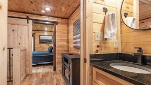 L’intérieur d’une cabane en bois comprend un lit, une petite cuisine, une salle de bain avec un lavabo et un miroir, et une porte qui donne sur une autre pièce.