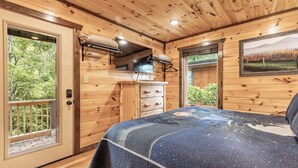 Une chambre dans une cabane en bois, avec un lit, une commode et une grande fenêtre.