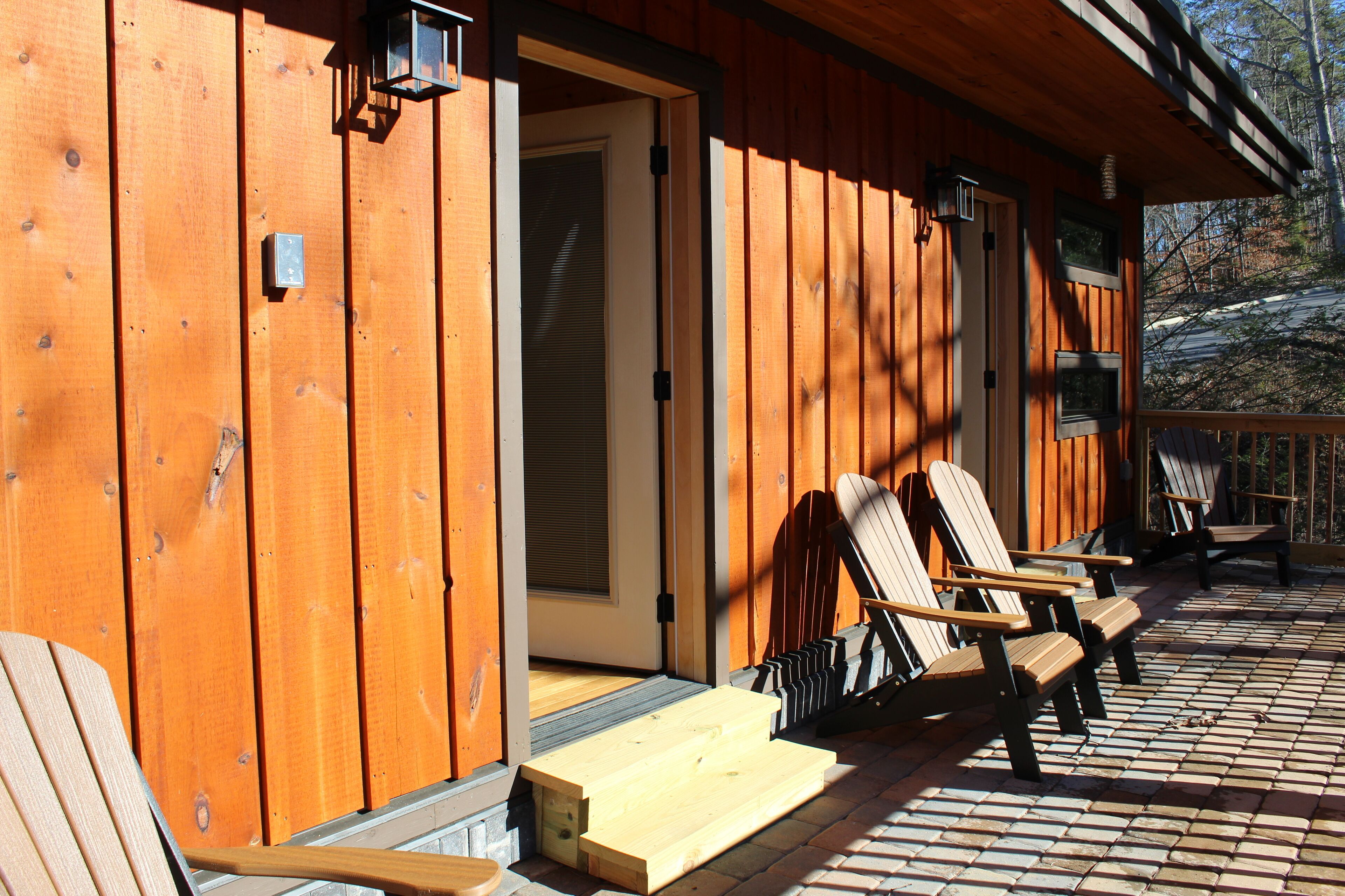 A wooden cabin with a porch, a door, and three Adirondack chairs.