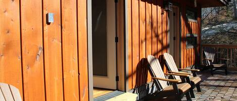 A wooden cabin with a porch, a door, and three Adirondack chairs.
