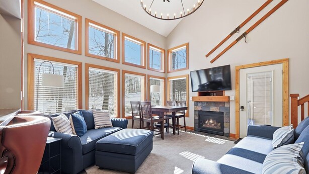 A spacious living room with a fireplace, large windows, a television, and a dining area. - Ski In/Out| Combined Upper and Lower Unit 780/781 | 5 Bedroom | Gas Fireplace (Boyne Fallss)