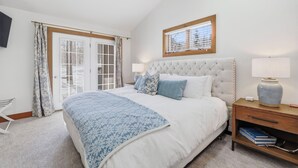 A bedroom with a large bed, a bedside table with a lamp, a window with blinds, and a door with curtains. - Ski In/Out| Combined Upper and Lower Unit 780/781 | 5 Bedroom | Gas Fireplace (Boyne Fallss)