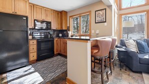 A modern kitchen with wooden cabinets, a black refrigerator, and a central island with bar stools. - Ski In/Out| Combined Upper and Lower Unit 780/781 | 5 Bedroom | Gas Fireplace (Boyne Fallss)