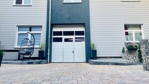 A two-story house with a garage door, a balcony, and a stone wall with plants.