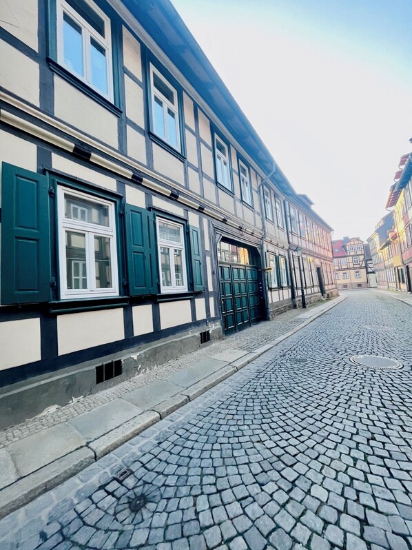 A cobblestone street lined with traditional half-timbered buildings with green shutters.