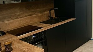 A modern kitchen with a wooden countertop, black cabinets, a built-in microwave, and a dishwasher.
