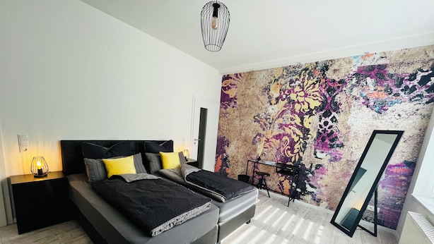 A modern bedroom with a large bed, bedside tables, a desk, and a vibrant abstract mural.