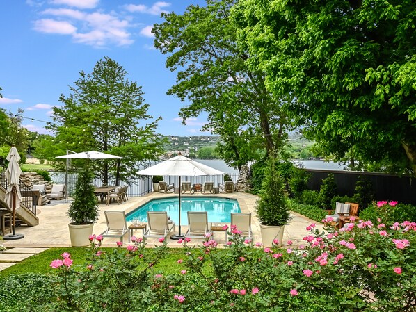 A backyard with a swimming pool, surrounded by lush greenery and pink flowers. - Above Austin Icon | Waterfront Lake Austin | Pool l Sauna l Game Rm I Family (Austin)