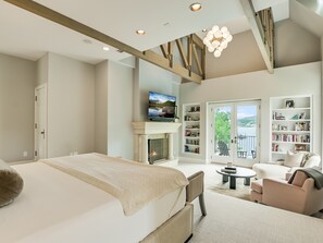 A modern bedroom with a large bed, a fireplace, a television, and a balcony with a view. - Above Austin Icon | Waterfront Lake Austin | Pool l Sauna l Game Rm I Family (Austin)